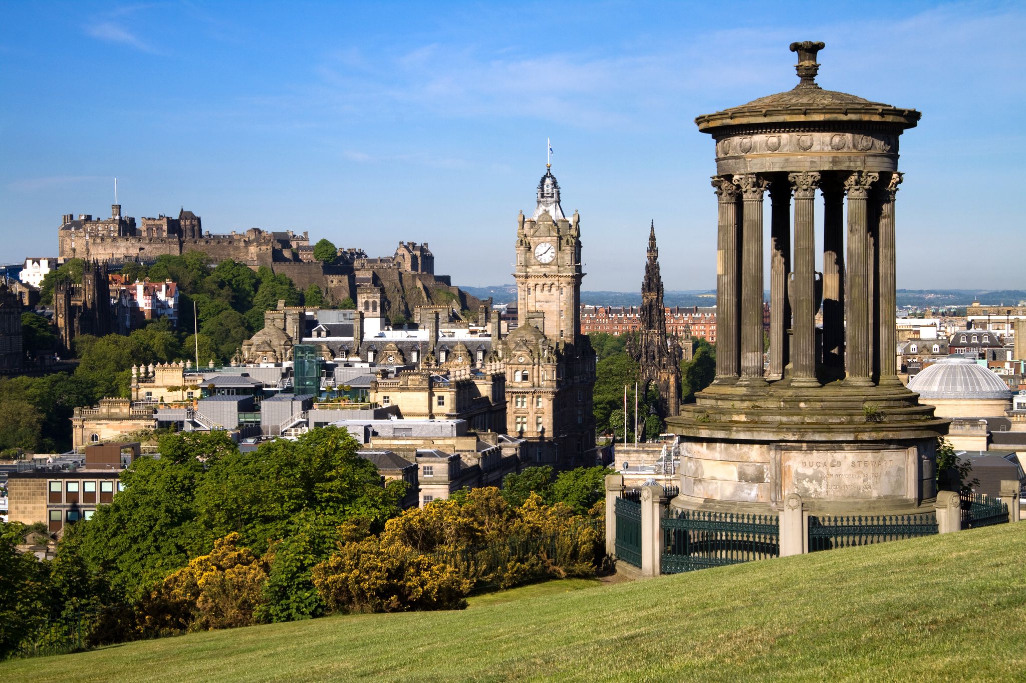 Photo of Edinburgh City and Castle, Scotland, viewed from Calton Hill on a beautiful summer morning with the Dugald Stewart monument in the foreground, Scott monument and Balmoral clock tower in background.