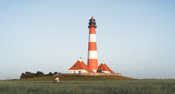 photo of view of girl with a bicycle on the of Westerheversand Lighthouse in Germany.