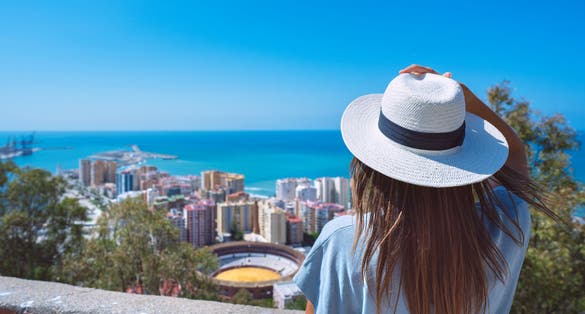 Photo of woman traveler in white sun hat enjoying view of Malaga city.
