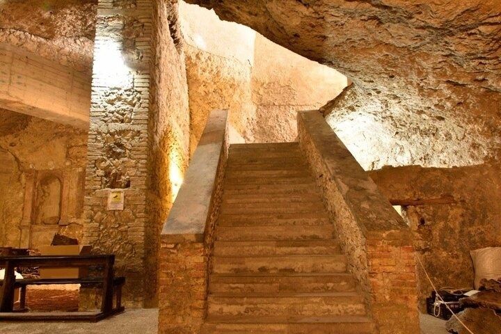 An old underground stone chamber in Cagliari with a central staircase, rustic walls, and warm lighting..jpg