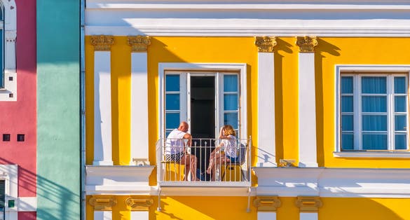 Man and woman sitting on a small balcony of an old colored building right in the center of Timisoara.