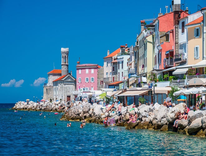 People swimming and sunbathing along the colorful seaside promenade in Piran, Slovenia, on a sunny day..jpg