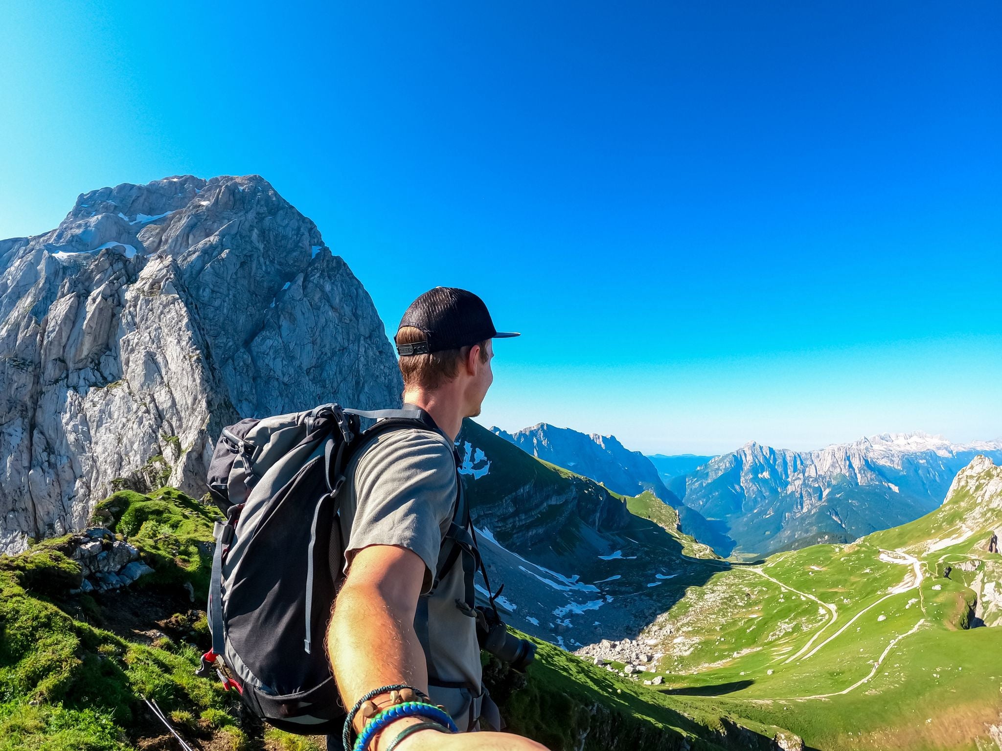 Photo of Man taking selfie with scenic view of high alpine Mangart road (Mangartska cesta) seen from Mangart Saddle (Mangartsko sedlo), Julian Alps, border Slovenia Italy.