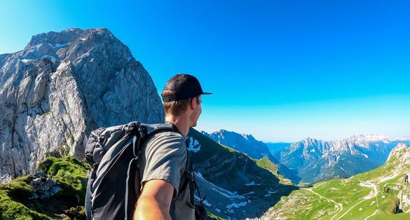 Photo of Man taking selfie with scenic view of high alpine Mangart road (Mangartska cesta) seen from Mangart Saddle (Mangartsko sedlo), Julian Alps, border Slovenia Italy.