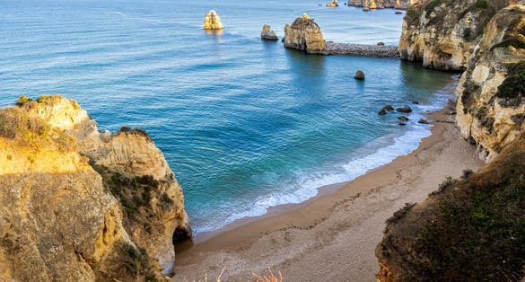 High angle view of the cliff's edge that adds a sense of height to Praia do Pinhao beach, also known as Baía dos Segredos, bathed in golden evening sun with the calm Atlantic Ocean in the background.