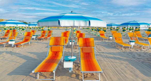 Photo of Blue umbrellas and chaise lounges on the beach of Rimini in Italy.