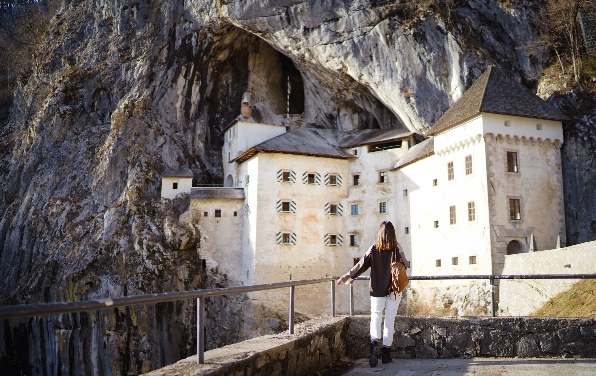 A traveler woman stands back to the camera and enjys view of Predjama Castle (Predjamski grad), a Renaissance castle built within a cave mouth in the historical region of Inner Carniola, Slovenia