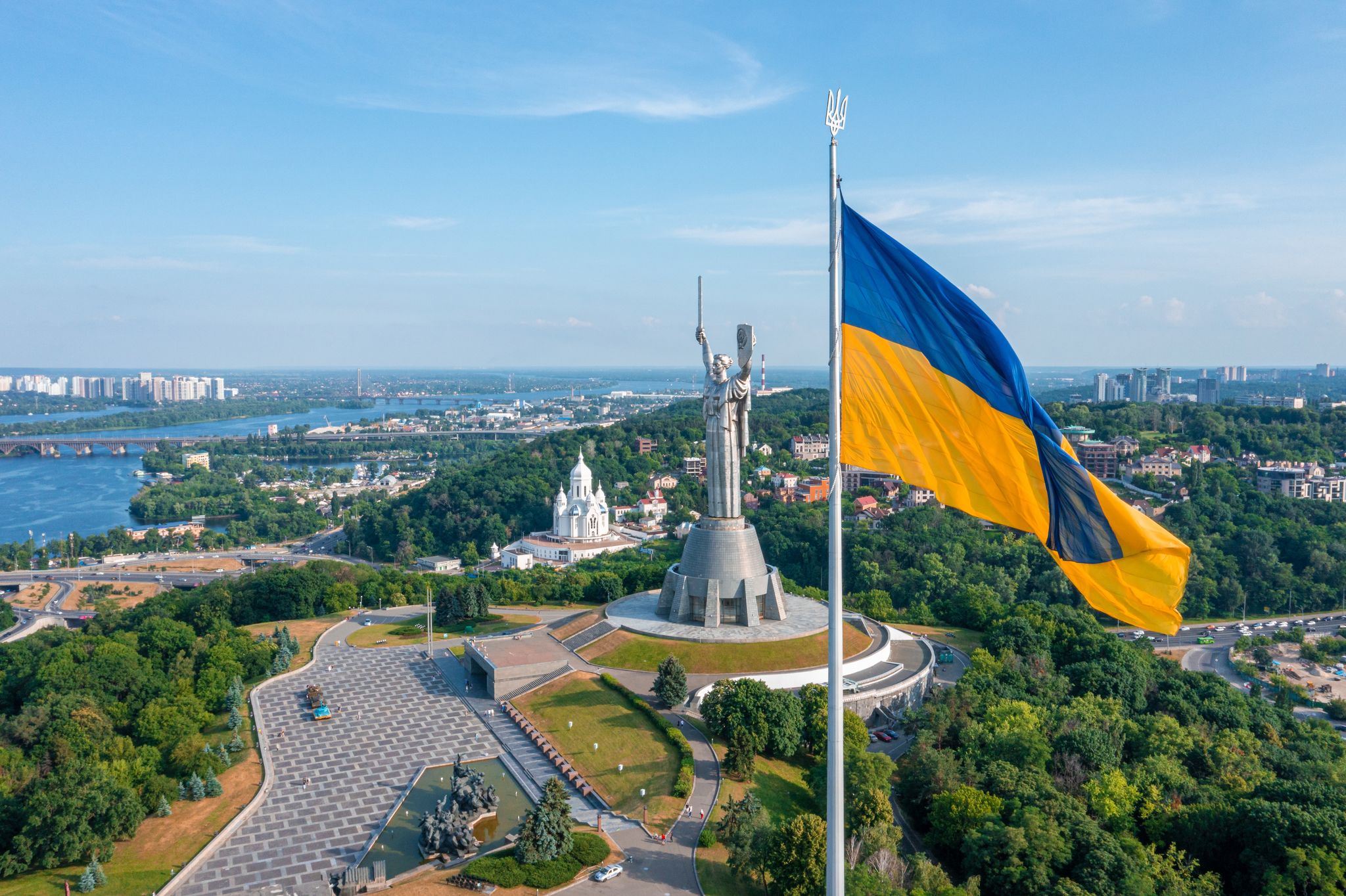 Photo of aerial view of the Ukrainian flag waving in the wind against the city of Kyiv, Ukraine near the famous statue of Motherland.