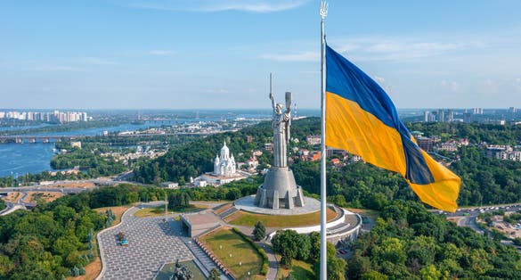 Photo of aerial view of the Ukrainian flag waving in the wind against the city of Kyiv, Ukraine near the famous statue of Motherland.