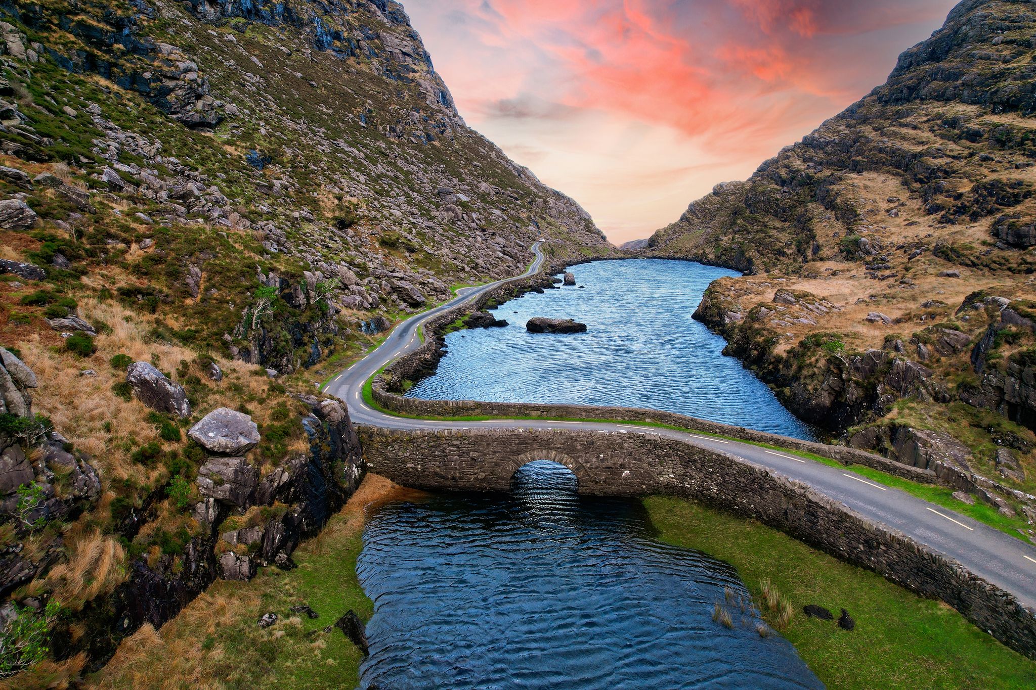 Aerial view of sunset at the stone Wishing Bridge over winding stream in green valley at Gap of Dunloe in Black Valley of Ring of Kerry, County Kerry, Ireland