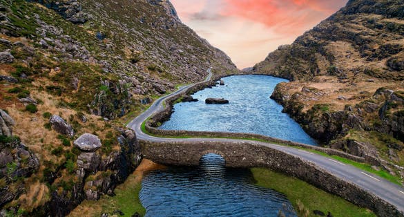 Aerial view of sunset at the stone Wishing Bridge over winding stream in green valley at Gap of Dunloe in Black Valley of Ring of Kerry, County Kerry, Ireland