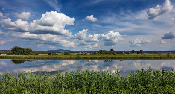 Photo of Dramatic clouds in blue sky reflect in the water of the the Rhine-Main-Danube Canal near Forchheim, Germany.