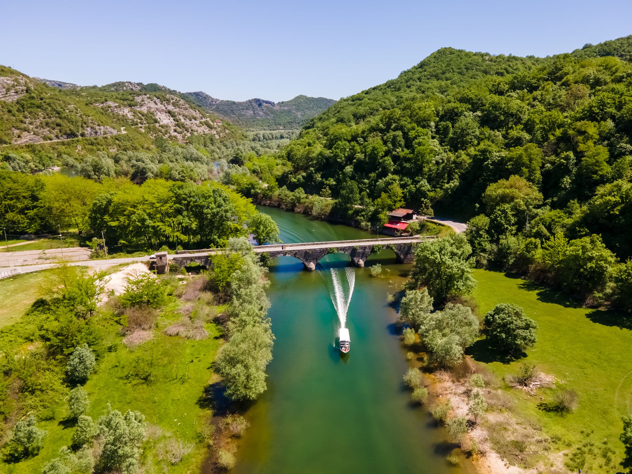Photo of aerial view of Rijeka Crnojevića bridge with a boat passing under it, in Montenegro.