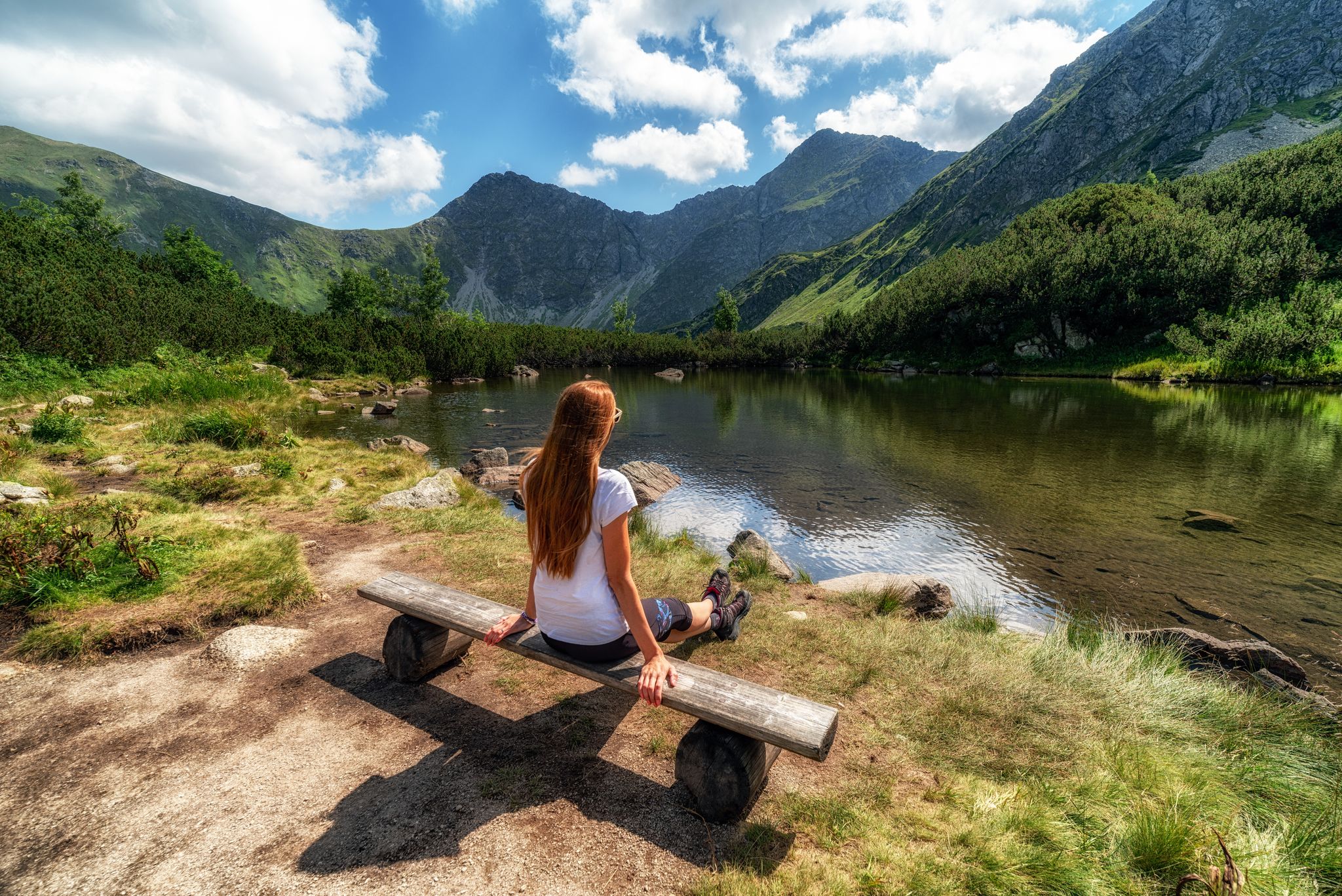 Photo of Girl tourist sitting on bench looking on beautiful nature with lake called Rohacske plesa and hill Volovec in summer mountains in Western Tatras in Slovakia.
