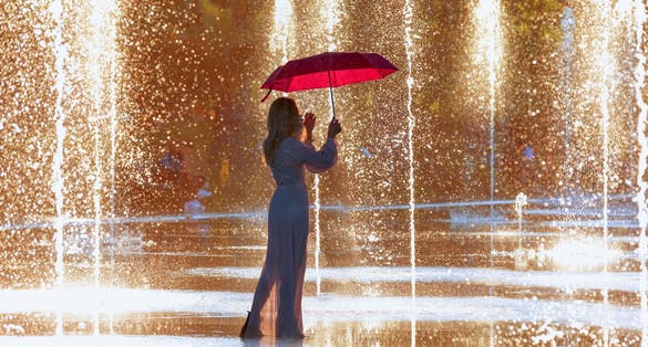 photo of young girl in white dress holding red umbrella and walking on the fountain at Picturesque Park Paillon Promenade in Nice, France.