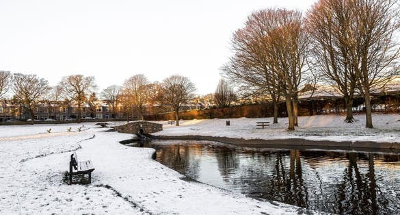 Westburn park with a small pond, stone bridge and bench during winter season, Aberdeen, Scotland