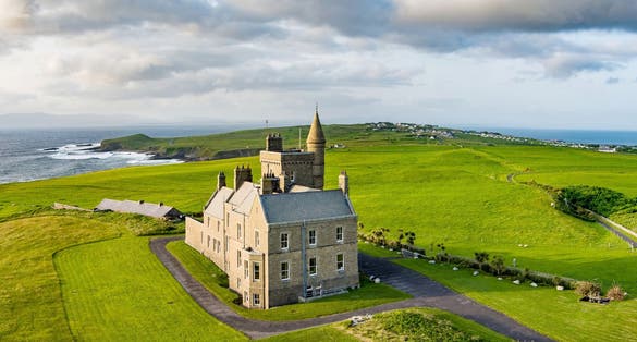Classiebawn Castle on a backdrop of picturesque landscape of Mullaghmore Head. Spectacular sunset view with huge waves rolling ashore. Signature point of Wild Atlantic Way, Co. Sligo, Ireland