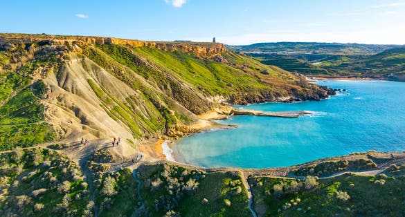 Nature landscape of Ghajn Tuffieha bay. Aerial view. People on the hill. Clear blue sky, sea and green grass. Malta island