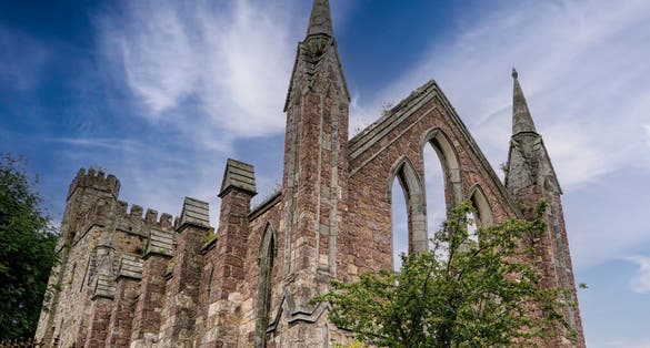 Photo of Front and perspective view of ruins of an old Gothic church in the Irish town of Wexford with blue sky and white clouds.