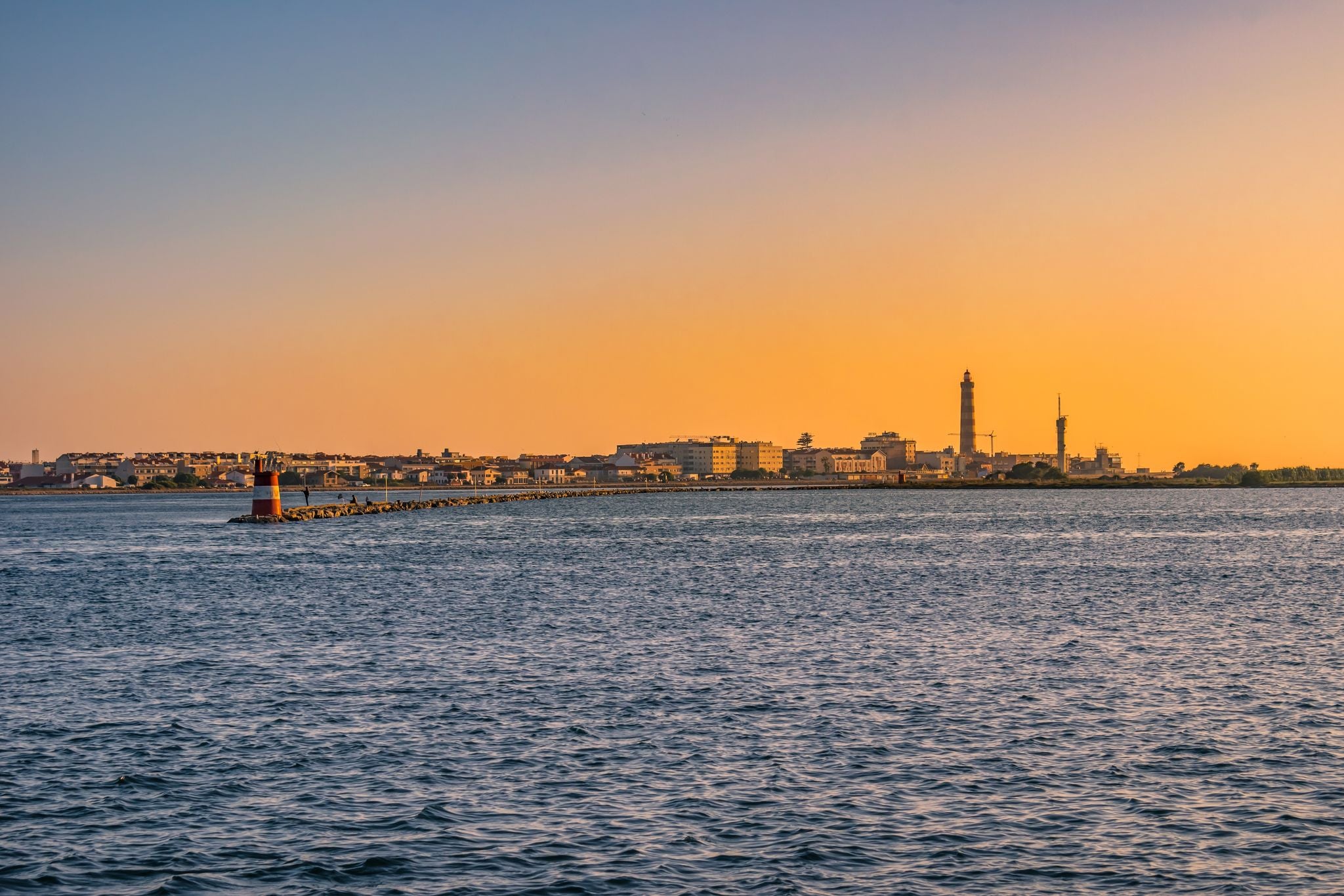 Breakwater of Aveiro estuary with buildings and Barra lighthouse in the horizon at golden hour, Gafanha da Nazaré PORTUGAL