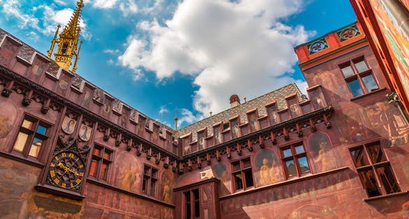 photo of great low-angle view of the inner courtyard of the Town Hall in Basel. It is characteristic for its colorful roof, red façade, frescoes, reliefs, crenellations, the wall clock and the golden turret in Basel, Switzerland.