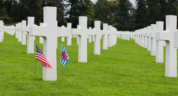 white crosses at an american cemetery, with an american and a luxembourg flag at one cross.