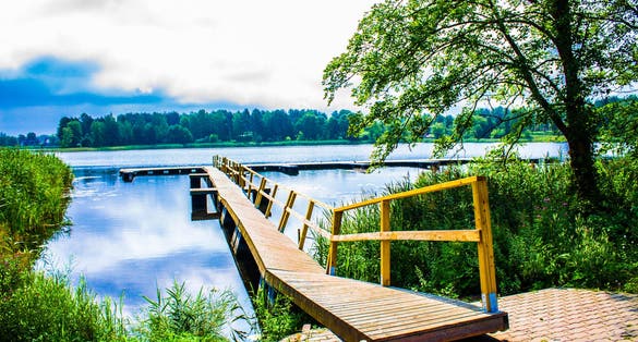 Beautiful lake park on a bright sunny summer day near Trakai Castle in Lithuania, Europe. Lake Galvė is a lake in Trakai Lithuania. Lake and Forest Panorama, blue sky, yellow boat dock.