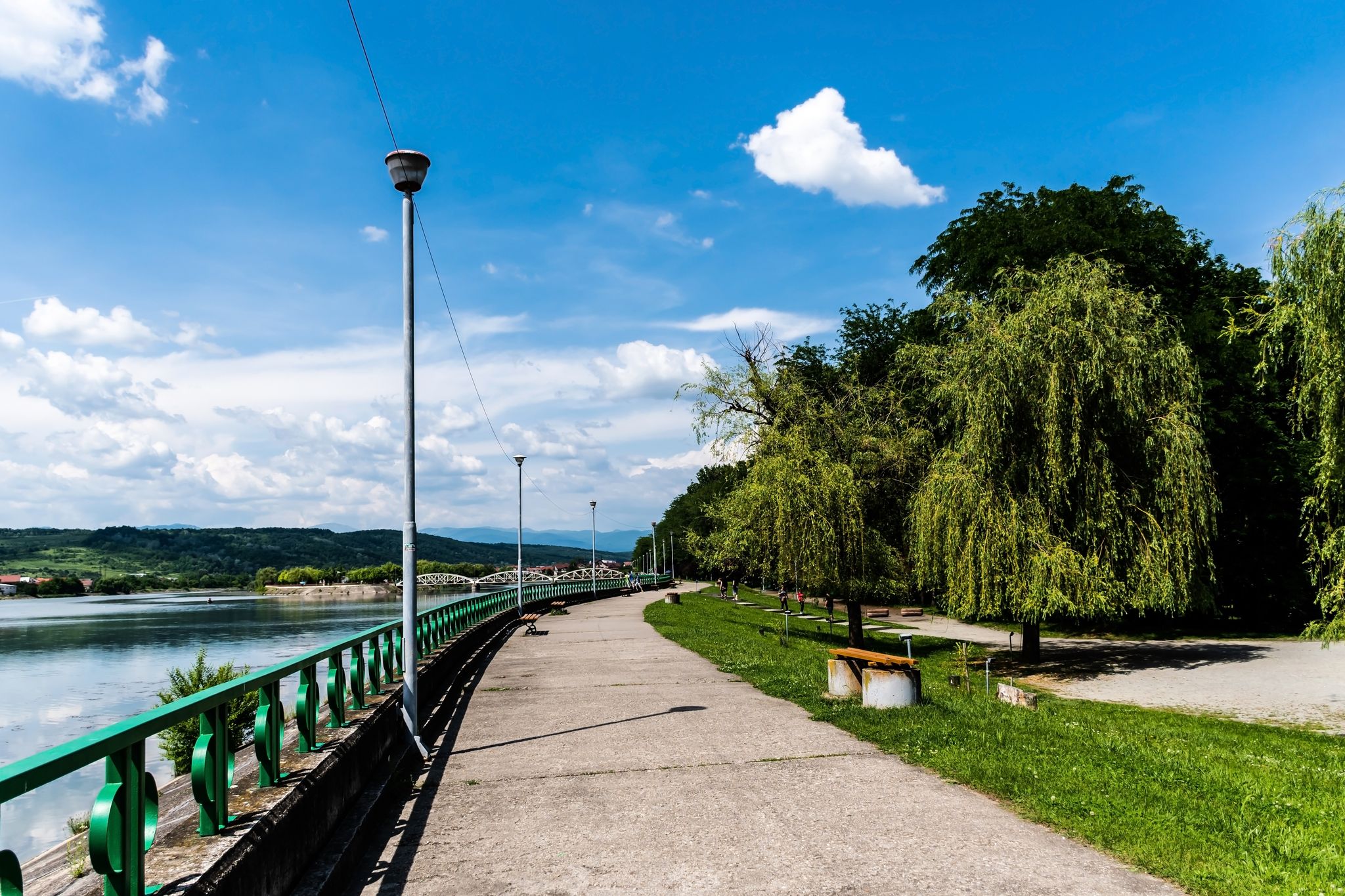 The alley in Targu Jiu central park next the Jiu river and in the background is the old bridge over the Jiu, also called Ferdinand's bridge. Targu jiu, Romania.