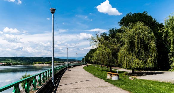 The alley in Targu Jiu central park next the Jiu river and in the background is the old bridge over the Jiu, also called Ferdinand's bridge. Targu jiu, Romania.