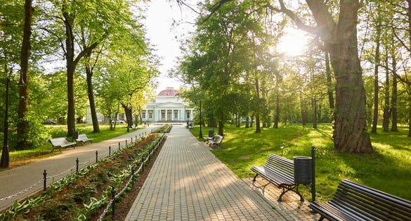 photo of view of Alley in city park. Benches, floral decoration, bicycle road, trees, flowers, plants. Liepaja, Latvia. Summer landscape. Public places, urban planning, landscaping design, gardening, recreation themes