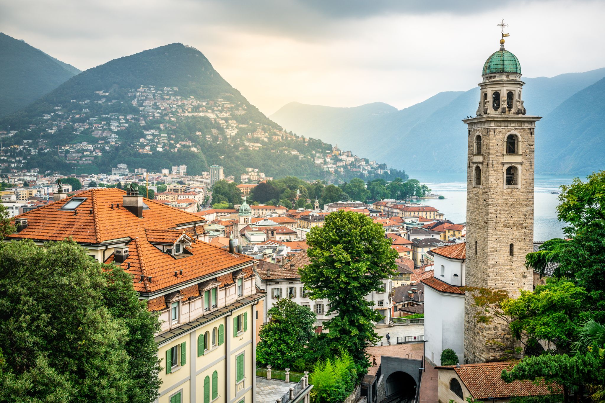 photo of aerial cityscape of Lugano with Cathedral of Saint Lawrence bell tower and lake view and dramatic light in Lugano Ticino Switzerland.