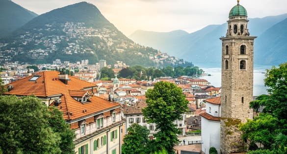 photo of aerial cityscape of Lugano with Cathedral of Saint Lawrence bell tower and lake view and dramatic light in Lugano Ticino Switzerland.