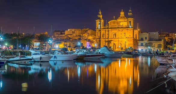 Photo of Msida, Malta - The beautiful Msida Parish Church with yachts and boats and reflection on the water by night.