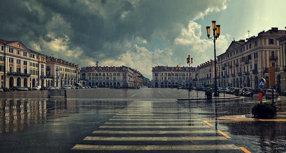 photo of Pedestrian crossing and big plaza at city center under cloudy sky at rainy day in Cuneo, Italy.