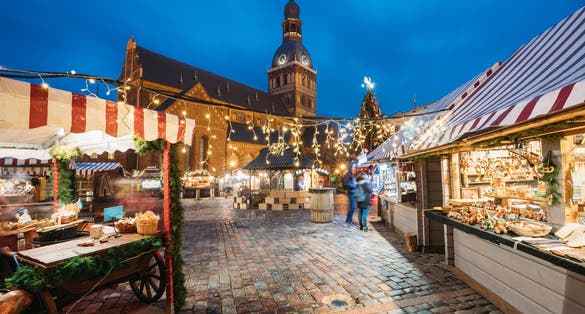 photo of Riga, Latvia. Christmas market on dome square with Riga dome cathedral. Christmas tree and trading houses. Famous landmark at winter xmas evening night In Illuminations Light.