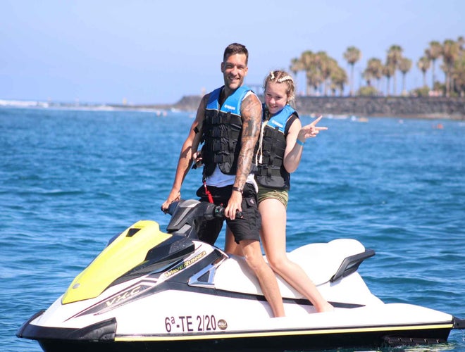 A man and a woman wearing life jackets ride a jet ski in the blue waters of Costa Adeje, Tenerife, on a sunny day..jpg