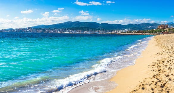 Photo of the beautiful beach in Palma de Mallorca with the town and harbor in background, beautiful coastline
