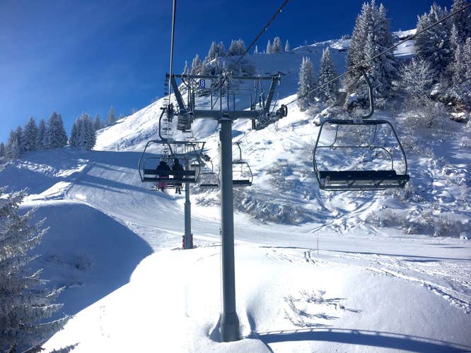 Photo of ski chair lift in Praz Sur Arly in the French Alps on a sunny day in the snow .