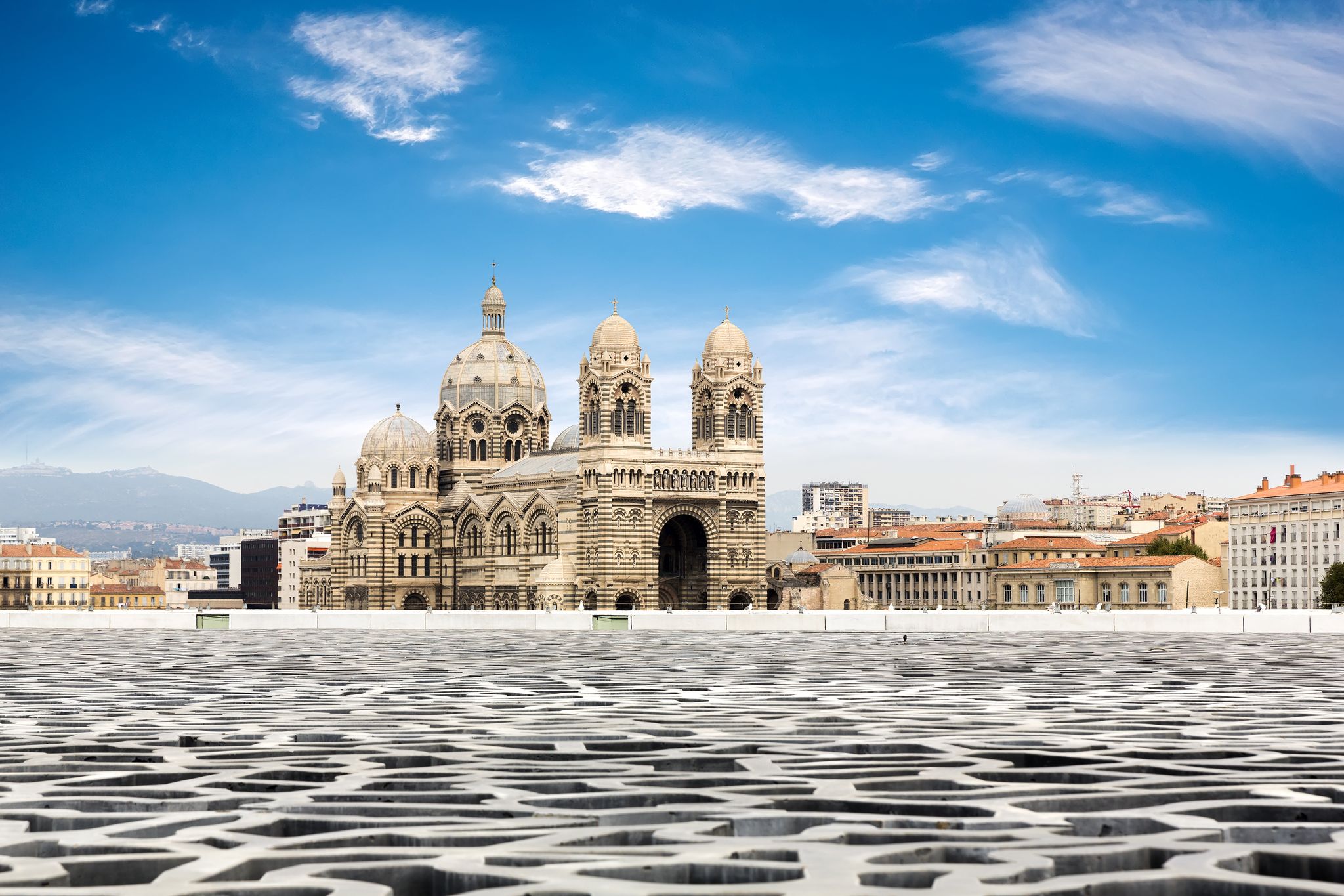 View of Marseille Cathedral (Cathédrale La Major) with the patterned rooftop of Mucem foreground, under a blue sky in Marseille, France..jpg