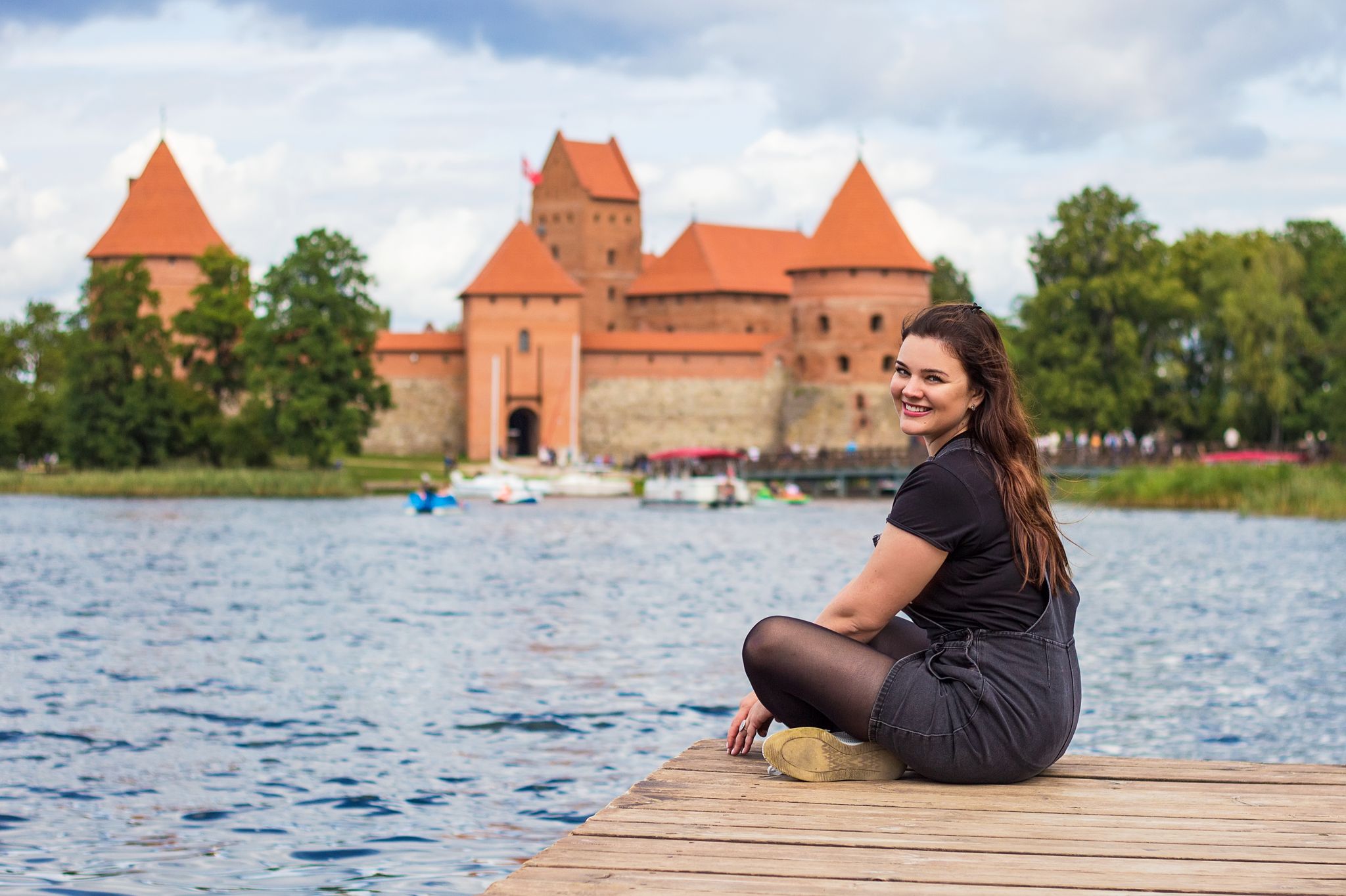 photo of beautiful young smiling woman posing on the shore of galve lake, tourist traveler near trakai Island castle, Lithuania. Lithuanian sights, travel to the baltic countries.