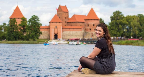 photo of beautiful young smiling woman posing on the shore of galve lake, tourist traveler near trakai Island castle, Lithuania. Lithuanian sights, travel to the baltic countries.