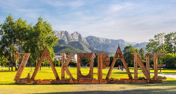 Wooden letters - landmark sign with the name of the city. Panoramic scenic landscape view of High Tatra Mountains peaks and Giewont in background. Rowien Krupowa park, Zakopane, Poland.