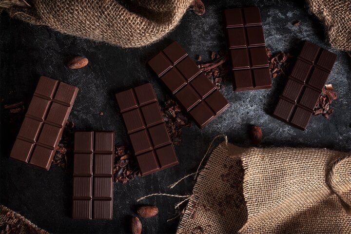 Several dark chocolate bars are placed on a black surface with cocoa beans and burlap fabric around them..jpg