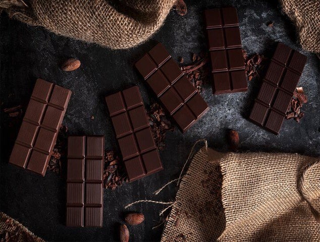Several dark chocolate bars are placed on a black surface with cocoa beans and burlap fabric around them..jpg
