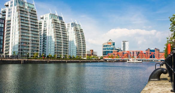 photo of tall modern apartment buildings quayside overlooking canal and bridge. Shot at beautiful morning in Salford Quays, Manchester, England.