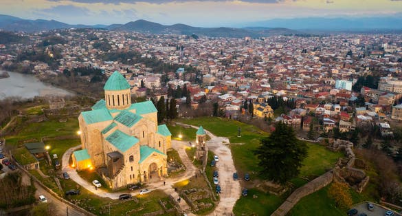 Photo of drone of illuminated rebuilt building of Cathedral of Dormition, temple of Georgian Orthodox Church in Kutaisi against cityscape on spring evening.