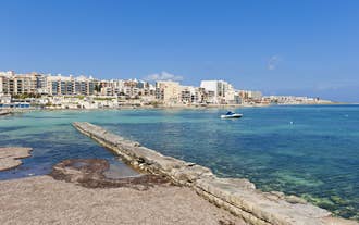 Photo of aerial view of seaside cliffs, colourful houses and streets of Qawra town in St. Paul's Bay area in the Northern Region, Malta.