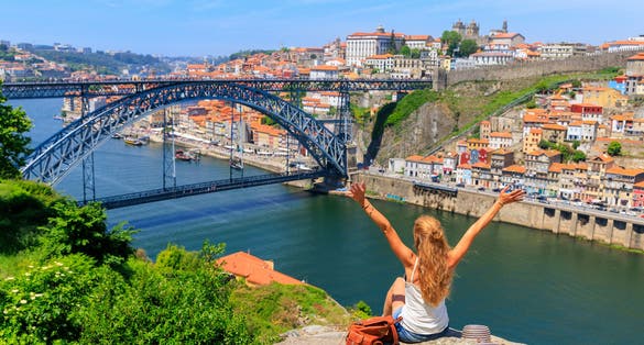 Photo of woman tourist with arms raised enjoying beautiful panoramic view of famous iron bridge and old town Porto, Portugal.