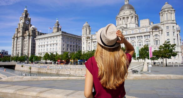 Photo of tourist woman visiting Pier Head with "The Three Graces" in the city centre of Liverpool, England.
