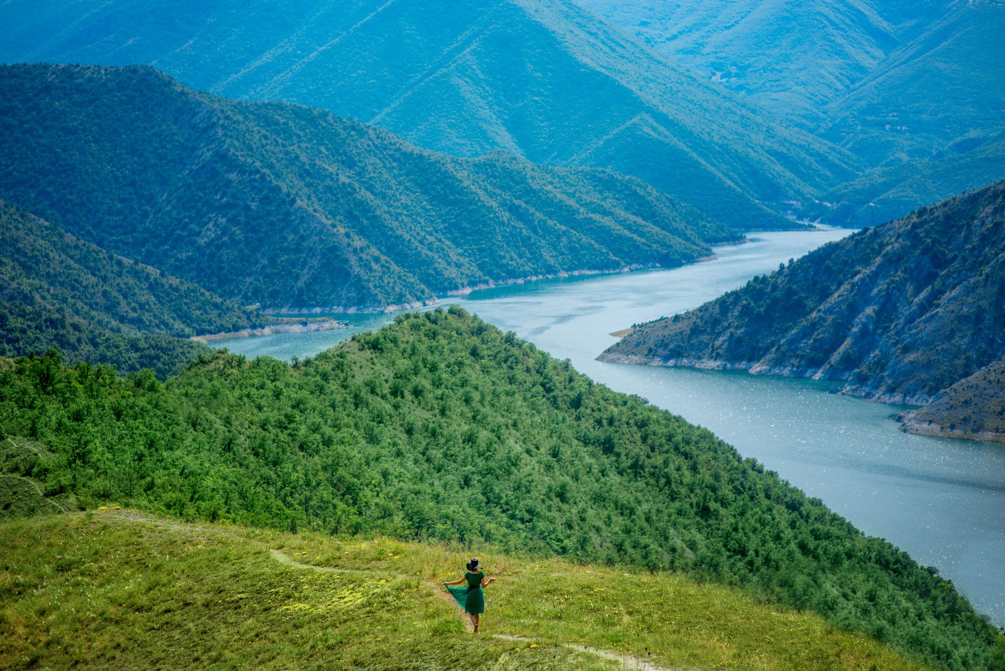 Photo of a woman in front of beautiful blue green Kozjak lake surrounded by hills in the mountains of North Macedonia.